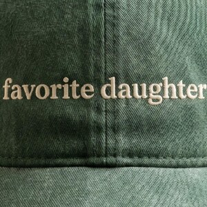 K&ouml;nnte beinhalten: Dunkelgr&uuml;ne Baseballkappe mit dem gestickten Text "favorite daughter" in hellem Beige. Die Kappe besteht aus einem strukturierten Stoff und hat einen gebogenen Schirm.