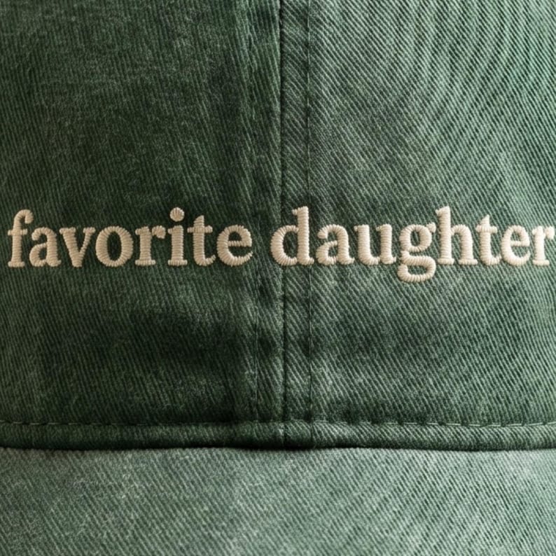 K&ouml;nnte beinhalten: Dunkelgr&uuml;ne Baseballkappe mit dem gestickten Text "favorite daughter" in hellem Beige. Die Kappe besteht aus einem strukturierten Stoff und hat einen gebogenen Schirm.