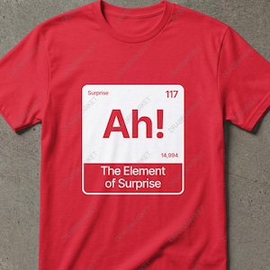Peut inclure: Un t-shirt rouge avec un motif carré blanc. Le motif comprend le texte "Ah!" et "The Element of Surprise", stylisé comme un élément du tableau périodique. Le t-shirt est à col rond et à manches courtes.
