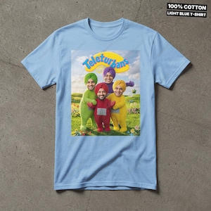 Pode incluir: Uma t-shirt de manga curta azul-clara com uma impress&atilde;o gr&aacute;fica de quatro figuras em trajes coloridos com turbantes num campo relvado. O texto Teleturbans est&aacute; impresso acima das figuras. A t-shirt &eacute; 100% algod&atilde;o.