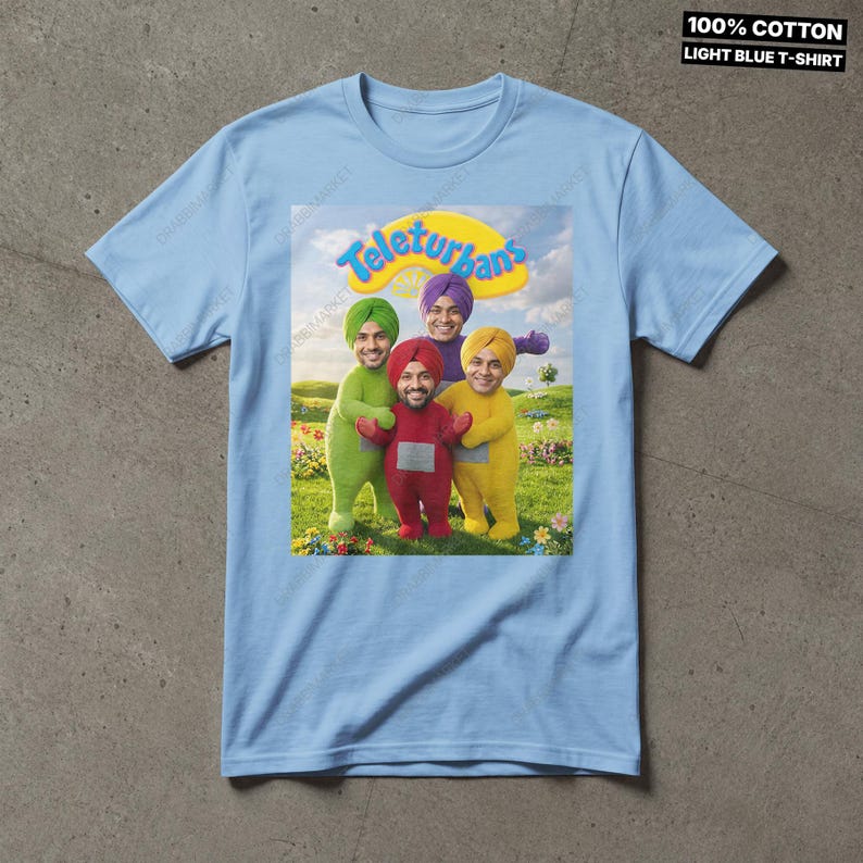 Pode incluir: Uma t-shirt de manga curta azul-clara com uma impress&atilde;o gr&aacute;fica de quatro figuras em trajes coloridos com turbantes num campo relvado. O texto Teleturbans est&aacute; impresso acima das figuras. A t-shirt &eacute; 100% algod&atilde;o.