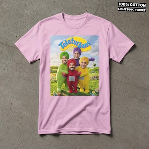 Pode incluir: Uma t-shirt de manga curta rosa claro com uma impress&atilde;o gr&aacute;fica de quatro figuras em trajes verdes, vermelhos, roxos e amarelos com turbantes num campo sob um c&eacute;u azul. O texto "Teleturbans" aparece acima. Inclui o texto "100% COTTON LIGHT PINK T-SHIRT".