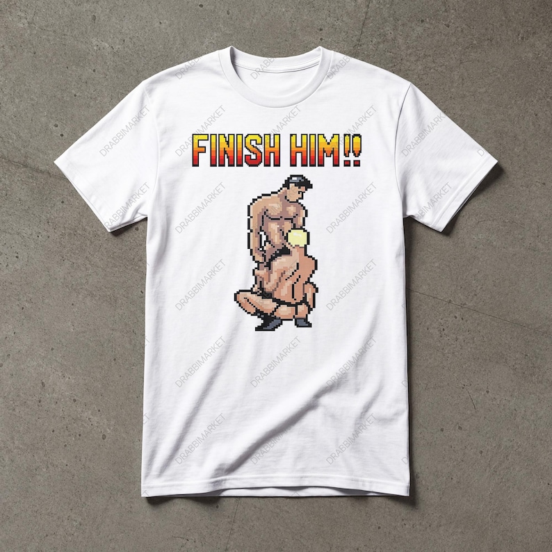 May include: A white short-sleeved t-shirt featuring a pixel art graphic of two figures in a sexual position. Above the graphic, the text FINISH HIM!! is printed in a yellow and red pixelated font. The shirt has a crew neckline and short sleeves.