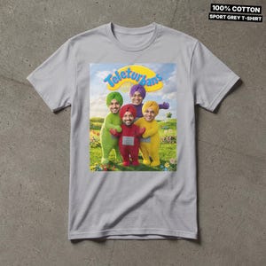 Pode incluir: Uma t-shirt cinzenta desportiva de 100% algod&atilde;o com uma impress&atilde;o gr&aacute;fica de quatro figuras em fatos verdes, vermelhos, roxos e amarelos com turbantes, num campo relvado sob um c&eacute;u azul. O texto Teleturbans est&aacute; impresso em amarelo.