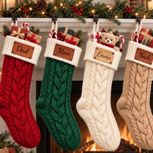 May include: Four cable-knit Christmas stockings in red, green, cream, and tan, each featuring a white ribbed cuff and a brown leather patch engraved with the names Dad, Mom, Emma, and Noah. The stockings are filled with small gifts and candy canes.