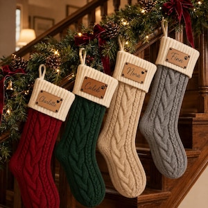 Peut inclure: Quatre chaussettes de Noël en tricot torsadé de couleur rouge, vert foncé, beige et gris. Chaque chaussette possède un revers crème avec une étiquette en cuir rectangulaire gravée des prénoms Charlotte, Caleb, Nora et Finn, avec des cœurs ou pattes.