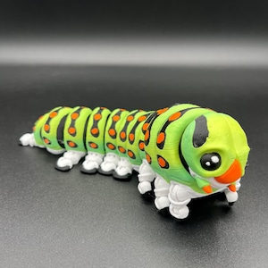 May include: A segmented caterpillar figurine featuring a vibrant green body with black stripes and bright orange circular spots. The creature has a rounded head with large black eyes, an orange nose, and multiple white articulated legs along its body.