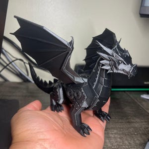 May include: A black, articulated dragon figurine featuring a mechanical aesthetic with visible gear-like details on its legs and body. The creature has large, pointed wings, a sharp, angular head, and a textured, segmented tail, all rendered in matte black.
