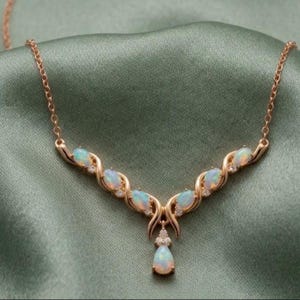 May include: A gold-toned necklace with opal gemstones and small clear crystals. The necklace has a teardrop-shaped opal pendant. The necklace is displayed on a green satin background.