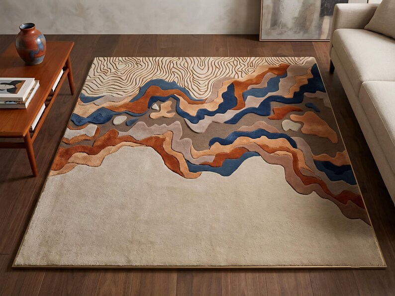 Puede incluir: Una alfombra rectangular con un dise&ntilde;o de paisaje ondulado y superpuesto en tonos crema, beige, naranja &oacute;xido, marr&oacute;n y azul oscuro. La secci&oacute;n superior muestra un fino patr&oacute;n topogr&aacute;fico lineal, mientras que la parte inferior es de color crema.
