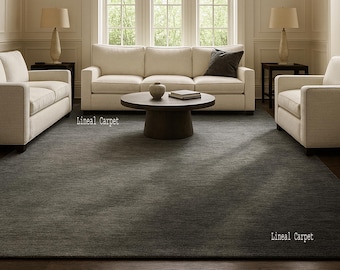 May include: A large, rectangular gray area rug in a living room setting. The rug is placed under a cream-colored sofa, two armchairs, and a round coffee table. The text "Lineal Carpet" is printed on the rug.