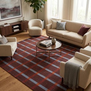 Puede incluir: Una alfombra rectangular grande con una base de color marrón oscuro y un patrón de cuadros prominente que consiste en rayas entrecruzadas de color azul claro y naranja. La alfombra se sitúa bajo una mesa de centro redonda de madera.