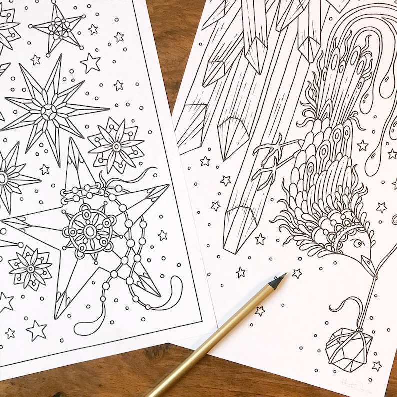 May include: Two detailed black and white coloring pages featuring celestial and geometric designs. One page showcases starbursts and star shapes, while the other depicts a bird-like figure and crystal formations. A gold pencil rests on the pages.