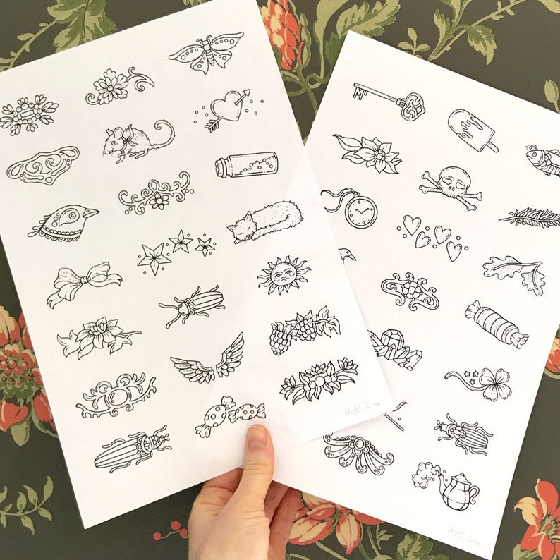 May include: Two sheets of paper with black and white illustrations of various designs. The designs include a butterfly, a heart with an arrow, a cat, a sun, a beetle, a bird, a bow, a flower, a bottle, a key, a skull, a fish, a clock, a candy, a leaf, a star, a wing, and more.