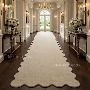 Puede incluir: Una larga alfombra de pasillo color crema con borde festoneado, colocada en un pasillo con suelo de madera oscura. El pasillo cuenta con espejos ornamentados, mesas y una lámpara de araña. El texto "ModernsCarpets" es visible en la alfombra.