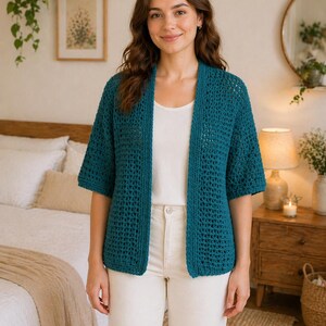 May include: A teal, open-front crochet cardigan with short sleeves. The cardigan is worn over a white top and paired with white pants. The open weave of the cardigan is visible.