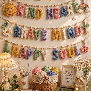 May include: A decorative wall hanging with the words "KIND HEART", "BRAVE MIND", and "HAPPY SOUL" crocheted in colorful yarn. The display includes a crocheted sun, rainbow, flowers, and a basket of yarn, creating a cozy, handmade aesthetic.
