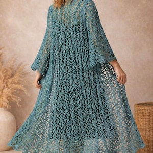 May include: A long, open-weave, teal crochet duster. The duster has long, flared sleeves and a scalloped hem. The garment is worn over a dark dress. The background is a neutral beige.
