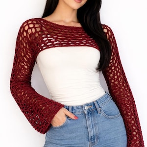 Puede incluir: Un bolero de ganchillo burdeos con mangas largas y un tejido abierto y ancho. El bolero se lleva sobre un top blanco y se combina con vaqueros azules. Las mangas tienen un diseño acampanado. El estilo general es bohemio.