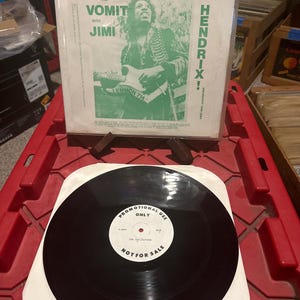 May include: A vinyl record with a black disc and a white label stating "PROMOTIONAL USE ONLY" and "NOT FOR SALE." The album cover displays a green and white graphic of Jimi Hendrix with the text "LET'S DROP SOME LUDES AND VOMIT WITH JIMI HENDRIX!"