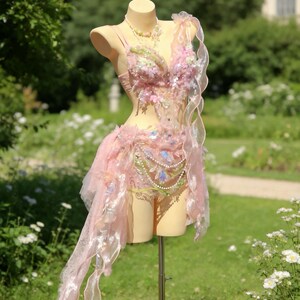 May include: A pink and white fantasy costume displayed on a mannequin. The costume features floral embellishments, sheer fabric, and pearl accents. The outfit includes a bodice, skirt, and decorative elements, creating a whimsical and ethereal aesthetic.