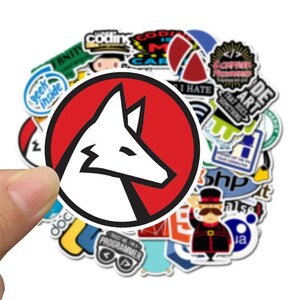 Peut inclure: Un ensemble d'autocollants color&eacute;s, dont un autocollant rond pro&eacute;minent avec une t&ecirc;te de renard blanche &agrave; l'int&eacute;rieur d'un cercle rouge. D'autres autocollants comportent des textes comme "Coding", "Geek Inside" et "Programmer".