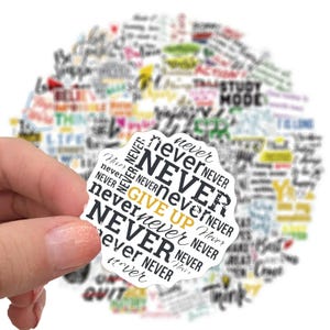 May include: A white sticker featuring the phrase "NEVER GIVE UP" in black and gold, encircled by the word "NEVER". The sticker is held in a hand, with a blurred backdrop of other motivational words and phrases.