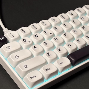 May include: A white mechanical keyboard with white keycaps and a dark purple space bar. The keyboard has a compact layout with a black "Esc" key and blue underglow lighting. The keys are labeled with letters, numbers, and symbols.