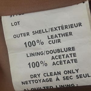 May include: Close-up of a garment label with text indicating the outer shell is 100% leather and the lining is 100% acetate. The label also states "Dry Clean Only".