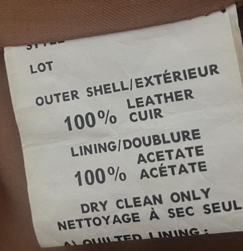 May include: Close-up of a garment label with text indicating the outer shell is 100% leather and the lining is 100% acetate. The label also states "Dry Clean Only".