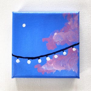Può includere: Piccolo dipinto quadrato su tela raffigurante una scena notturna. Il cielo è blu brillante, con una luna bianca e nuvole rosa. Una fila di luci bianche attraversa la tela.
