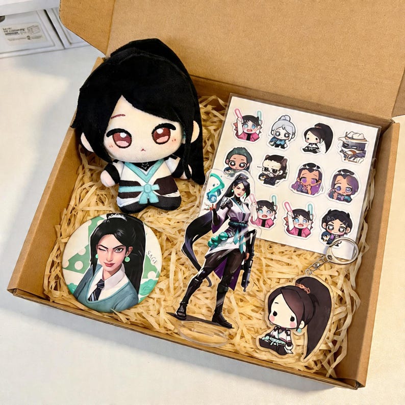 May include: A gift box filled with merchandise featuring a character with black hair. The box contains a plush doll, a button, a clear acrylic standee, a sheet of stickers, and a keychain. The items are arranged on a bed of straw.