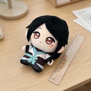 May include: A plush doll with black hair and large, expressive eyes. The doll wears a black and white outfit with a teal accent. A clear ruler, marked in centimeters, is next to the doll.