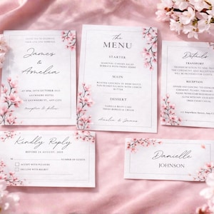 May include: A set of wedding stationery with a floral design. The invitation, menu, details, reply card, and place card feature pink cherry blossoms and elegant typography on a white background. The stationery is arranged on a pink fabric.