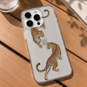 May include: A clear phone case featuring two illustrated leopards with brown and black spots. The case has a rectangular cutout for a triple-lens camera system and a circular cutout for the Apple logo on the back of the smartphone device.