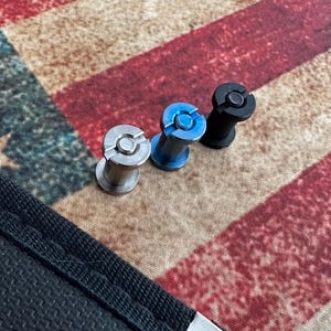 May include: Three metal objects with a cylindrical design. One is silver, one is blue, and one is black. Each has a circular top with a slot. The objects are on a patterned surface with red, white, and brown colors.