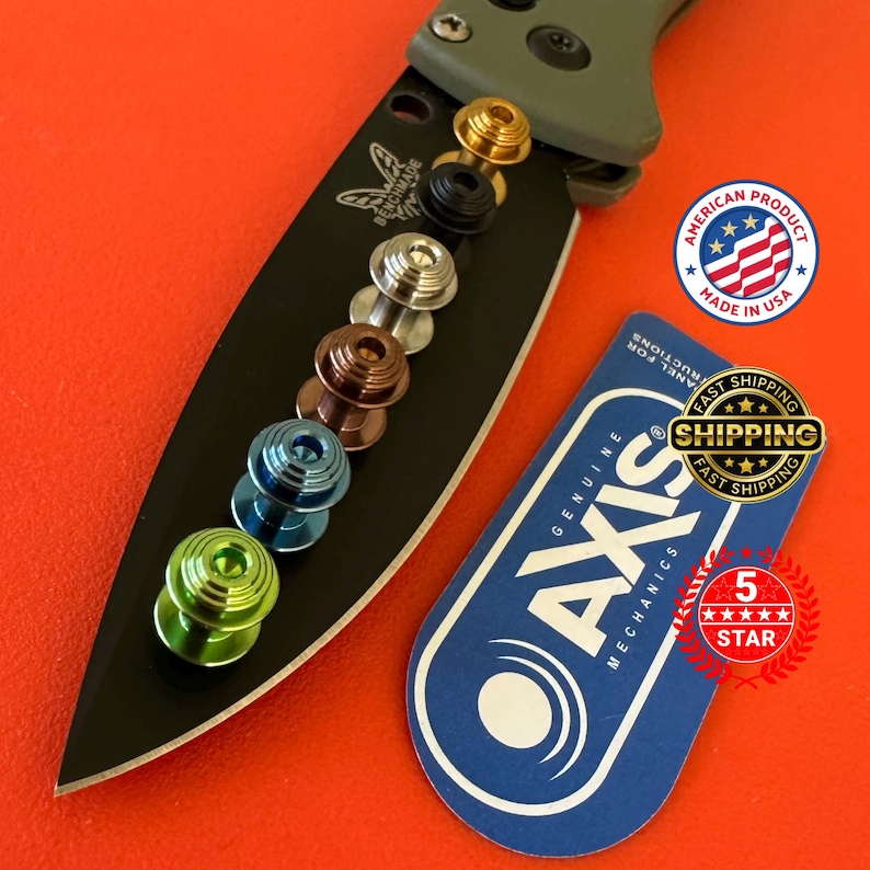 May include: A black Benchmade knife blade with a series of colorful thumb studs in gold, black, silver, bronze, blue, and green. The knife is set against an orange background. A blue tag with the text "AXIS MECHANICS" is also present.