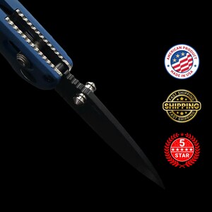 Puede incluir: Primer plano de una navaja negra con mango azul. La hoja es afilada y puntiaguda. El cuchillo tiene un tornillo plateado y un borde dentado. La imagen incluye el texto "AMERICAN PRODUCT MADE IN USA", "FAST SHIPPING" y "5 STAR".