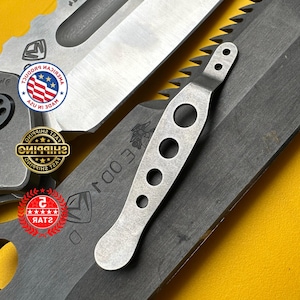 May include: Close-up of a collection of tactical knives. The blades are dark gray with a serrated edge on one. A silver-colored tool with three holes and a handle is also visible. The background is yellow.