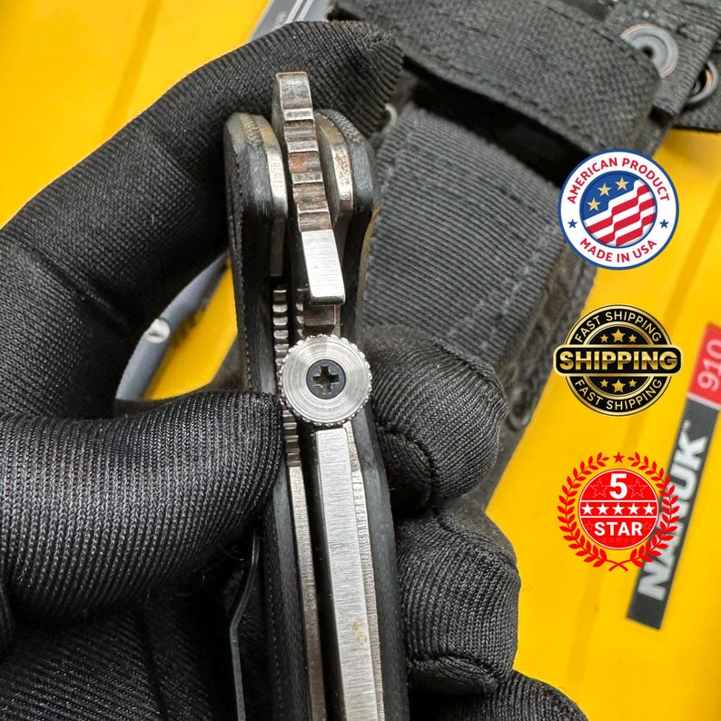 May include: Close-up of a partially open folding knife with a black handle and a silver blade. The knife is held by a gloved hand. The image includes a "Made in USA" sticker and a "5 Star" sticker.