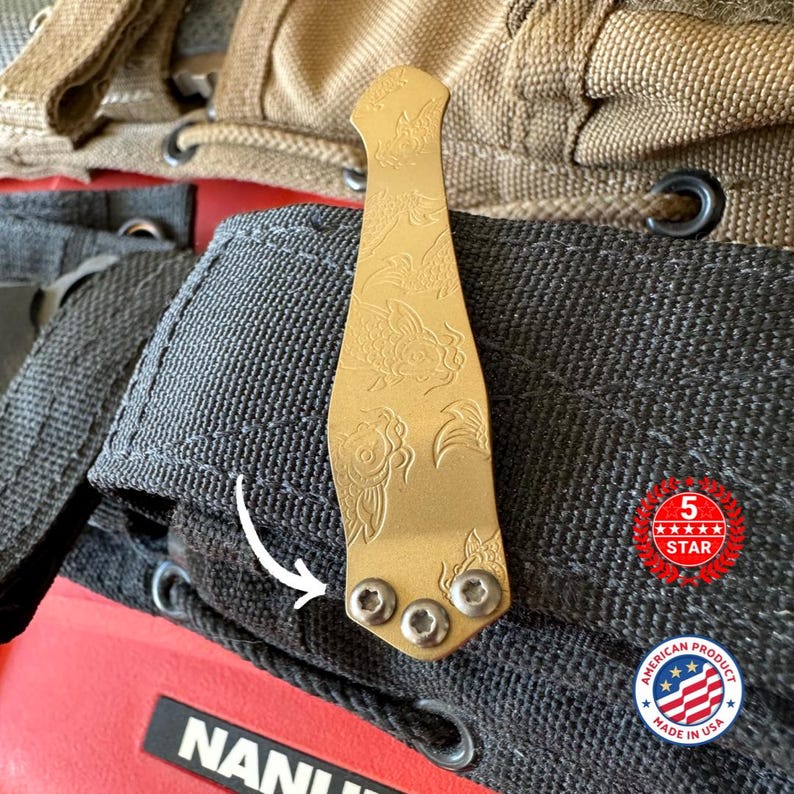 May include: A gold-colored metal clip with an engraved koi fish design. The clip is attached to a black fabric with three silver screws. The image also includes a "5 STAR" and "American Product Made in USA" sticker.