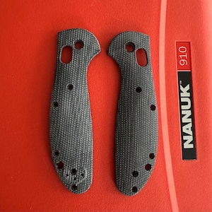 May include: Two gray, textured knife handle scales with multiple holes for attachment. The scales are made of a woven material and are shaped to fit a knife handle. The word "NANUK" is printed on a red background.
