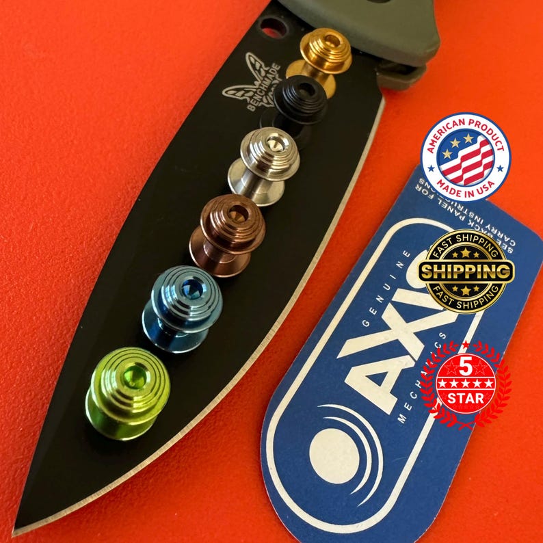 May include: A black knife blade with a series of colorful thumb studs in gold, black, silver, bronze, blue, and green. Includes a tag that says "Genuine AXIS Mechanics" and "Made in USA".