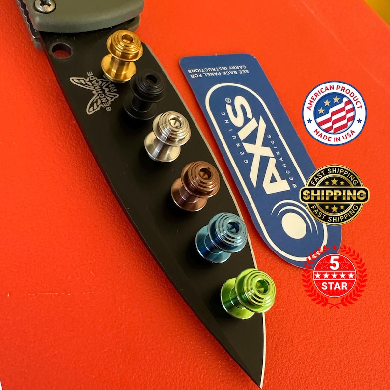 May include: A black Benchmade knife blade with a variety of colored thumb studs. The studs are gold, black, silver, copper, blue, and green. A blue and white Axis Mechanics card and an American product sticker are also present.