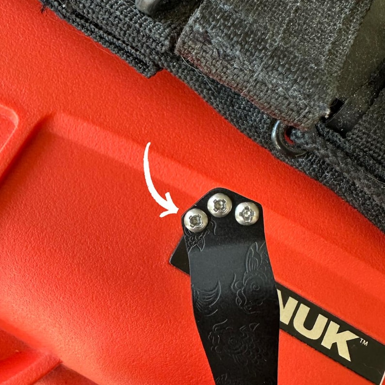 May include: Close-up of a black metal tool with three silver screws, attached to a red surface. The tool has a decorative floral design and the word "VUK" is visible.