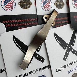 May include: A metallic knife hardware clip with a bronze finish. The clip has a curved shape. The background features business cards with knife graphics and the text "CUSTOM KNIFE HARDWARE Since 2018."