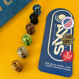 May include: A collection of multi-colored metal objects, including blue, black, bronze, green, silver, and gold. A blue and white card with the text "AKS MECHANICS" and "AMERICAN PRODUCT MADE IN USA" is also present.