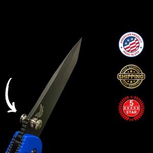 May include: A close-up shot of a black and silver folding knife with a blue handle. The blade is angled towards the viewer, with a butterfly logo. The knife is labeled "American Product Made in USA".