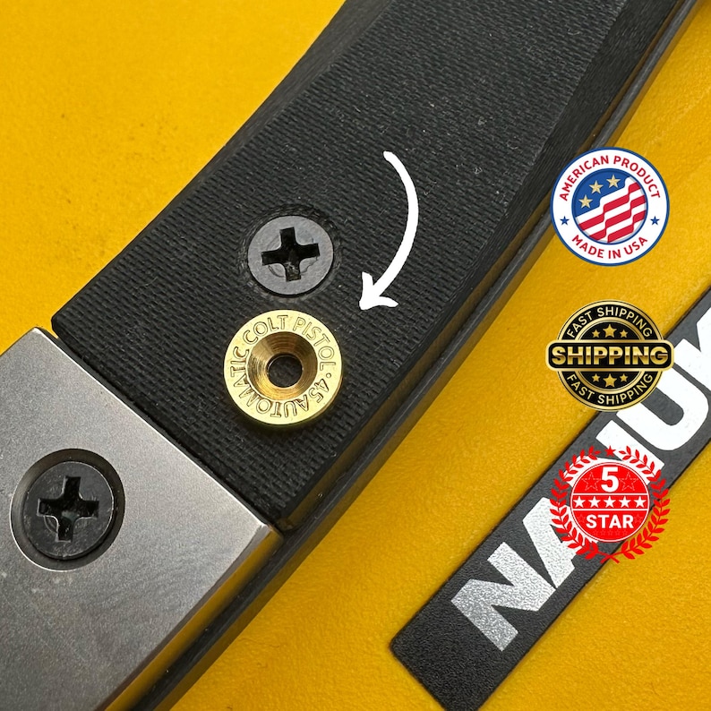 Pode incluir: Close-up de um objeto preto e prateado com uma superf&iacute;cie texturizada. Uma pe&ccedil;a dourada &eacute; gravada com "COLT PISTOL 45 AUTO". A imagem tamb&eacute;m inclui um adesivo "Made in USA" e um distintivo de "5 ESTRELAS".