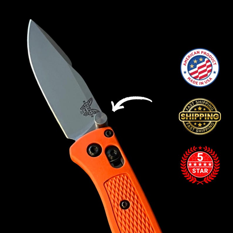 K&ouml;nnte beinhalten: Ein orangefarbenes Klappmesser mit silberner Klinge. Das Messer hat einen strukturierten Griff und ein Schmetterlingslogo auf der Klinge. Das Bild enth&auml;lt ein "Made in USA"-Abzeichen und ein "5 Sterne"-Abzeichen.